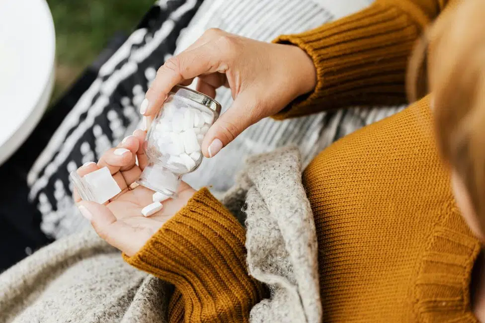 Pregnant woman holding Tylenol bottle and glass of water, considering safe dosage.