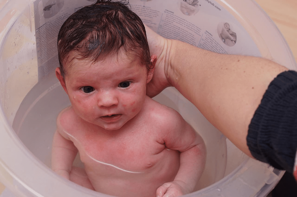 “Parent gently bathing a newborn baby in warm water with safe, proper newborn bath technique.”