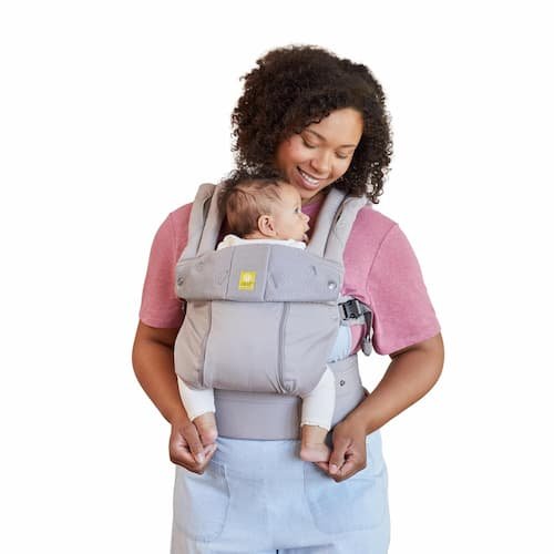 A mother wearing a LILLEbaby Complete All Seasons carrier in Stone gray, showcasing the wide ergonomic lumbar support panel and high-density nylon webbing adjusted for a plus-sized parental frame.