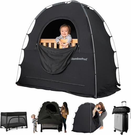 SlumberPod original blackout sleep tent travel cover assembled over a mini crib with a toddler looking out of the ventilated front window.