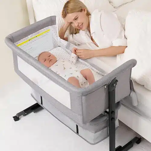 A mother sleeping peacefully next to her newborn in a 3-in-1 grey baby bassinet with breathable mesh, featuring height-adjustable settings for safe bedside sleeping.