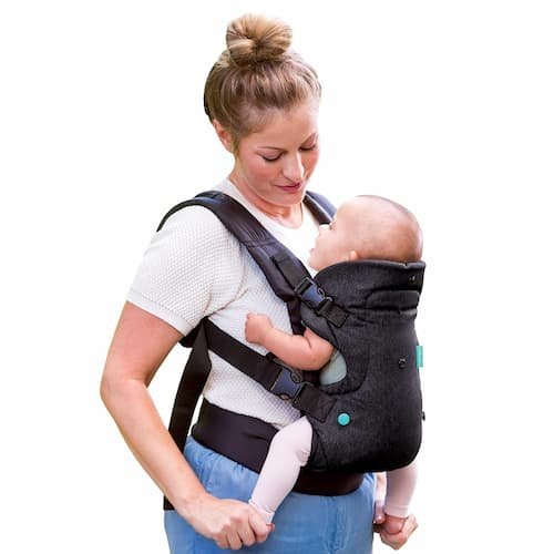 Infantino Flip 4-in-1 convertible baby carrier in black denim worn by a mother in front carry position showing adjustable straps.